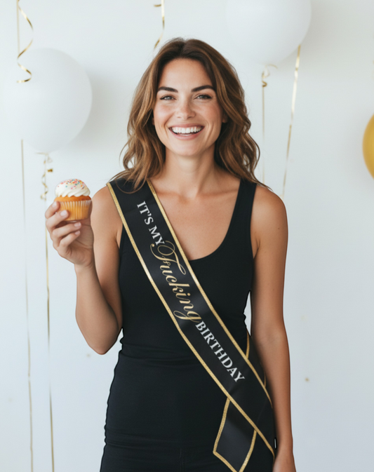 Littlegenie.com black satin birthday sash with gold foil text reading "IT'S MY FUCKING BIRTHDAY" and gold trim.